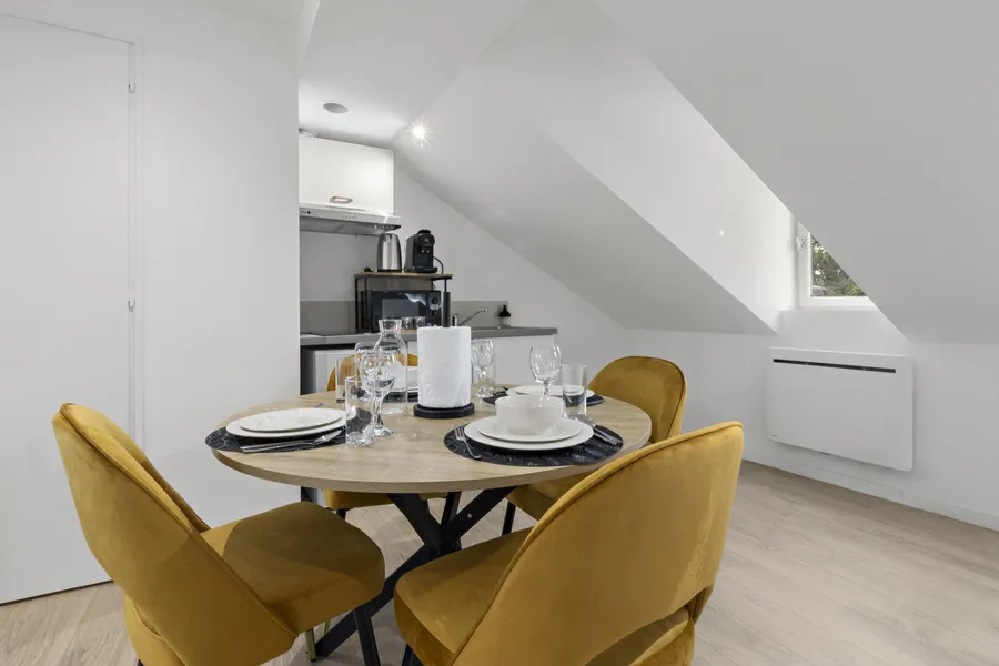 Coin repas d'un studio sous combles, table ronde en bois clair et chaises jaunes
